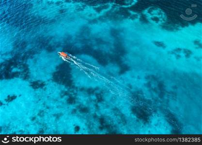 Aerial view of the fishing boat in clear blue water at sunset in summer. Top view from drone of yacht, sandy beach in Indian ocean. Travel in Zanzibar, Africa. Tropical landscape with motorboat, sea. Aerial view of the white boat in the clear blue water at sunset