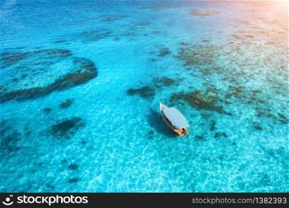 Aerial view of the fishing boat in clear blue water at sunset in summer. Top view from drone of yacht, sandy beach in Indian ocean. Travel in Zanzibar, Africa. Tropical landscape with motorboat, sea. Aerial view of the white boat in the clear blue water at sunset