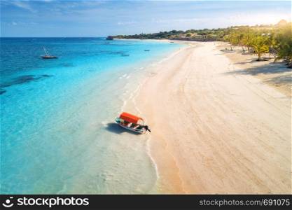 Aerial view of the fishing boat in clear blue water at sunset in summer. Top view of boat, sandy beach, palm trees. Indian ocean. Travel in Zanzibar, Africa. Colorful landscape with motorboat, sea