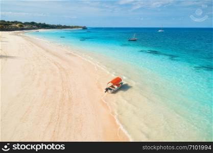 Aerial view of the fishing boat in clear blue water at sunset in summer. Top view of boat, sandy beach, palm trees. Indian ocean. Travel in Zanzibar, Africa. Colorful landscape with motorboat, sea