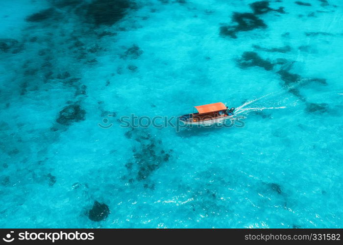 Aerial view of the fishing boat in transparent blue water at sunny day in summer. Top view from drone of floating boat in Indian ocean in Zanzibar, Africa. Landscape with yacht in clear sea. Seascape