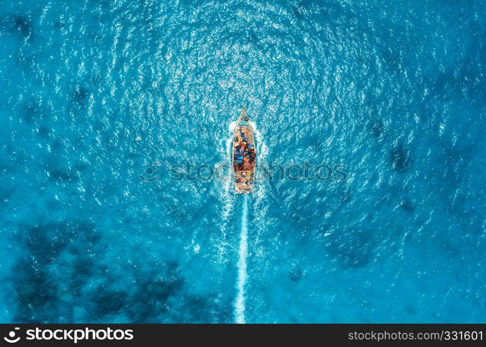 Aerial view of the fishing boat in transparent blue water at sunny day in summer. Top view from drone of floating boat in Indian ocean in Zanzibar, Africa. Landscape with yacht in clear sea. Seascape