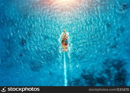 Aerial view of the fishing boat in transparent blue water at sunset in summer. Top view from drone of floating boat in Indian ocean in Zanzibar, Africa. Landscape with yacht in clear sea. Seascape