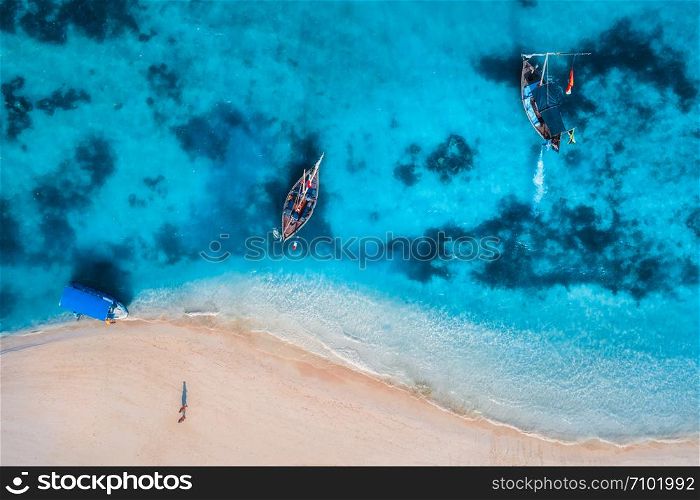 Aerial view of the fishing boats in clear azure water at sunrise in summer. Top view from drone of boat, blue sea, sandy beach, walking people. Indian ocean. Travel. Tropical seascape with motorboat
