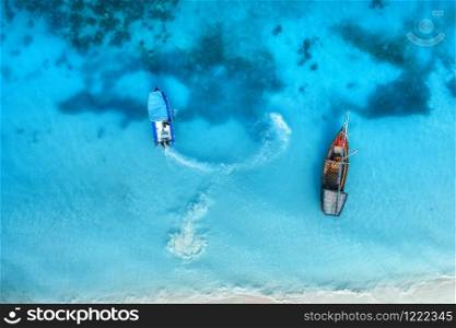 Aerial view of the fishing boats in clear blue sea at sunset in summer. Top view from drone of boat and yacht, sandy beach. Travel in Zanzibar, Africa. Tropical landscape with sailboats, azure water