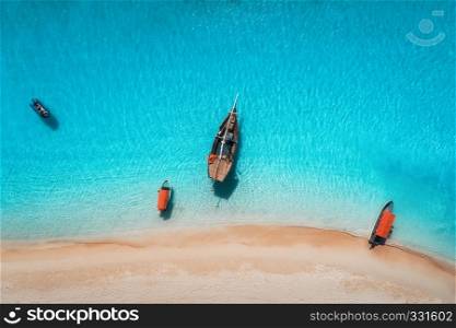 Aerial view of the fishing boats in clear blue water at sunny day in summer. Top view from drone of boat, sandy beach. Indian ocean in Zanzibar, Africa. Landscape with sailboats, clear sea. Seascape