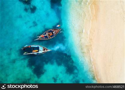 Aerial view of the fishing boats in clear blue water at sunset in summer. Top view from drone of boat, sandy beach. Indian ocean. Travel in Zanzibar, Africa. Tropical landscape with sailboats, sea