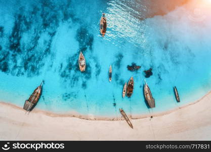 Aerial view of the fishing boats in clear blue water at sunset in summer. Top view from drone of boat, sandy beach. Indian ocean. Travel in Zanzibar, Africa. Tropical landscape with sailboats, sea. Aerial view of the fishing boats in clear blue water at sunset