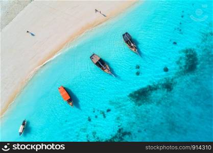 Aerial view of the fishing boats in clear blue water at sunset in summer. Top view from drone of boat, yacht, sandy beach. Indian ocean. Travel. Tropical seascape with sailboats, sea. View from above