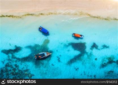 Aerial view of the fishing boats in clear blue water at sunset in summer. Top view from drone of boat, yacht, sandy beach. Indian ocean. Travel. Tropical seascape with sailboats, sea. View from above