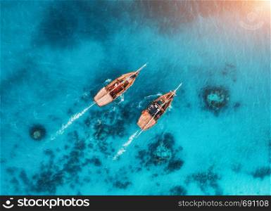 Aerial view of the fishing boats in transparent blue water at sunset in summer. Top view from drone of floating boat in Indian ocean in Zanzibar, Africa. Landscape with yacht in clear sea. Seascape