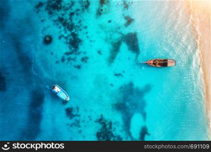 Aerial view of the fishing boats in transparent blue water at sunset in summer. Top view from of boat and sandy beach. Indian ocean in Zanzibar, Africa. Landscape with yachts and clear sea. Travel