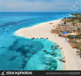 Aerial view of the fishing boats on tropical sea coast with sandy beach at sunset. Summer holiday in Zanzibar, Africa. Landscape with boat, yachts, palm trees, clear blue water and hotels. Top view