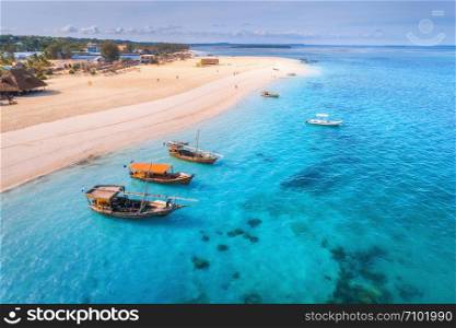 Aerial view of the fishing boats on tropical sea coast with sandy beach at sunset. Summer holiday on Indian Ocean, Zanzibar, Africa. Landscape with boat, palm trees, transparent blue water. Top view