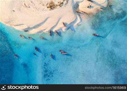 Aerial view of the fishing boats on tropical sea coast with white sandy beach at sunset. Summer travel in Zanzibar, Africa. Landscape with boats, yachts, green palm trees, clear blue water. Top view