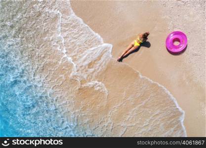 Aerial view of the lying beautiful young woman with pink swim ring on the sandy beach near sea with waves at sunset. Summer vacation in Lefkada island, Greece. Top view of sexy girl, clear blue water