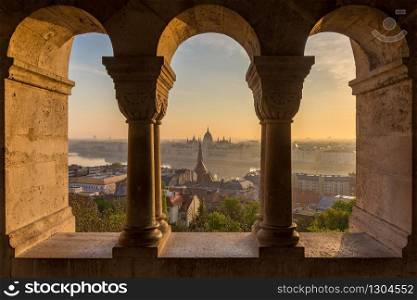 Aerial view of the Parliament of Hungary through Gothic windows of Fisherman&rsquo;s Bastion (Halaszbastya) at sunrise with beautiful sky and clouds , Budapest, Hungary