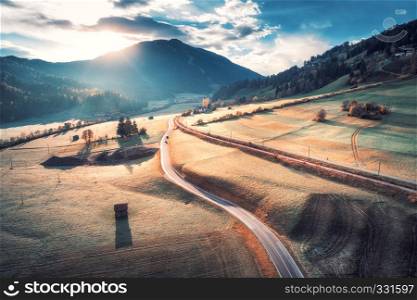 Aerial view of the road in mountain valley at sunset in Dolomites, Italy. Top view of asphalt roadway, meadows with grass and trees, buildings, hills in autumn. Highway and fields. Aerial landscape