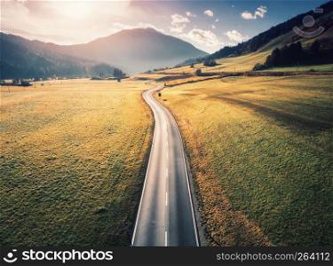 Aerial view of the road in mountain valley in Dolomites, Italy. Top view of perfect asphalt roadway, meadows with green grass, hills in autumn. Highway through the fields. Trip in europe. Travel