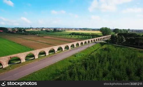 Aerial view of the Roman aqueduct in the mountains of Italy in Tuscany. White cars drive by road along the aqueduct