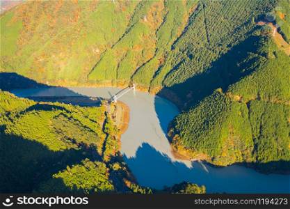 Aerial view of the steam train crossing Oigawa Railroad to go to station with red fall foliage in forest mountain hills and blue river in Autumn season, The red bridge in Shizuoka, Japan