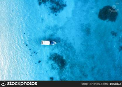 Aerial view of the white boat in the clear blue water at sunset in summer. Top view from drone of yacht, sandy beach in Indian ocean. Travel in Zanzibar, Africa. Tropical landscape with motorboat, sea