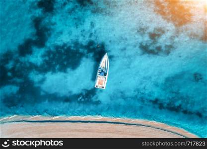 Aerial view of the white yacht in the clear blue water at sunset in summer. Top view from drone of boat, sandy beach. Indian ocean. Travel in Zanzibar, Africa. Tropical landscape with motorboat, sea. Aerial view of the white yacht in the clear blue water at sunset