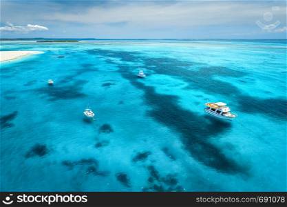 Aerial view of the yachts, fishing boats in transparent blue water at sunny day in summer. Top view of boat, sandy beach, sky. Travel in Zanzibar, Africa. Colorful landscape with motorboats in the sea