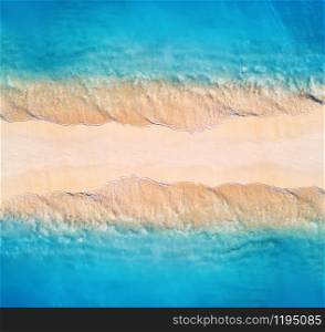 Aerial view of transparent blue sea with waves on the both sides and empty sandy beach at sunset. Summer holiday in Zanzibar, Africa. Tropical landscape with lagoon, white sand and ocean. Top view