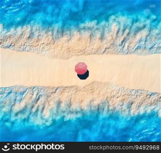 Aerial view of transparent blue sea with waves on the both sides and sandy beach with colorful red umbrella at sunset. Top view of sandbank. Summer travel. Tropical landscape with white sand and ocean