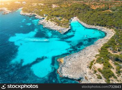 Aerial view of transparent sea with blue water, sandy beach, rocks, green trees, yachts and boats in sunny morning in summer. Travel in Mallorca, Balearic islands, Spain. Top view. Colorful landscape