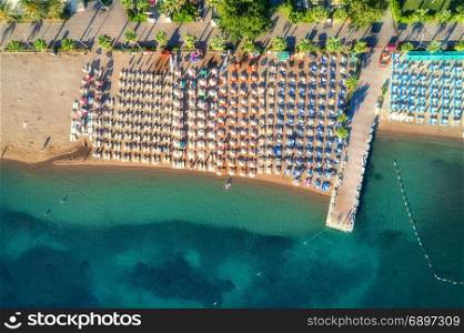Aerial view of transparent turquoise sea, beautiful sandy beach with colorful chaise-lounges, boats, green trees at sunset in Icmeler,Turkey. Summer seascape. Top view from flying drone. Azure water. Aerial view of transparent turquoise sea