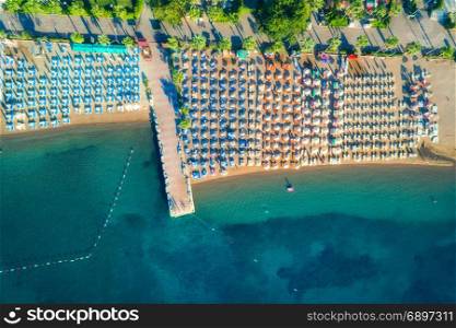 Aerial view of transparent turquoise sea, beautiful sandy beach with colorful chaise-lounges, boats, green trees, hotels, buildings at sunrise in Icmeler,Turkey. Summer seascape Top view from drone. Aerial view of transparent turquoise sea