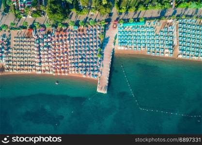 Aerial view of transparent turquoise sea, beautiful sandy beach with colorful chaise-lounges, boats, green trees at sunset in Icmeler,Turkey. Summer seascape. Top view from flying drone. Azure water