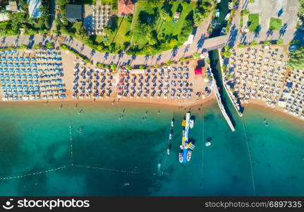 Aerial view of transparent turquoise sea, beautiful sandy beach with colorful chaise-lounges, boats, green trees, hotels, buildings at sunset in Icmeler, Turkey. Summer seascape Top view from drone