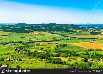 Aerial view of Tuscany natural landscape in summer with the cultivated land, the farm houses and a small city in the background