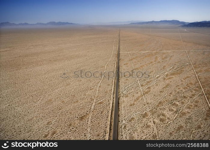 Aerial view of two lane highway in desert with mountains in background.