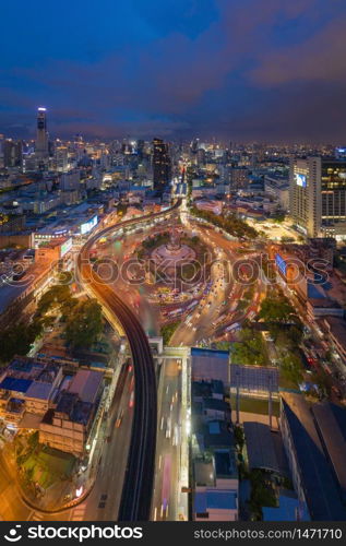 Aerial view of Victory Monument with car light trails on busy street road. Roundabout in Bangkok Downtown Skyline. Thailand. Financial district center in smart urban city. Skyscrapers at night.