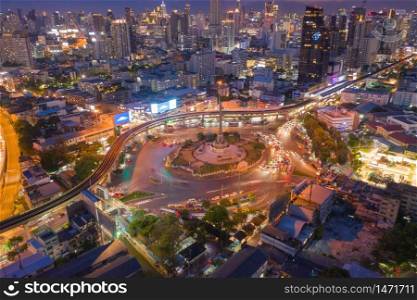 Aerial view of Victory Monument with car light trails on busy street road. Roundabout in Bangkok Downtown Skyline. Thailand. Financial district center in smart urban city. Skyscrapers at night.