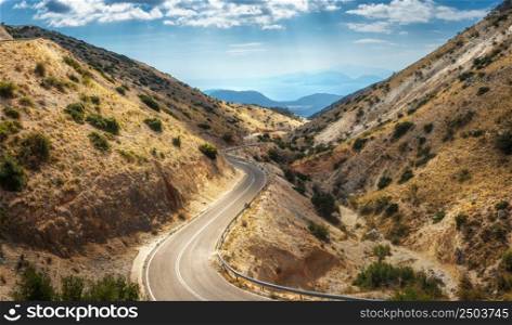 Aerial view of winding mountain road, blue sky with clouds at sunny day in summer. Lefkada, Greece. Top view of empty road, orange hills in spring. Beautiful landscape with highway. Panorama. Travel