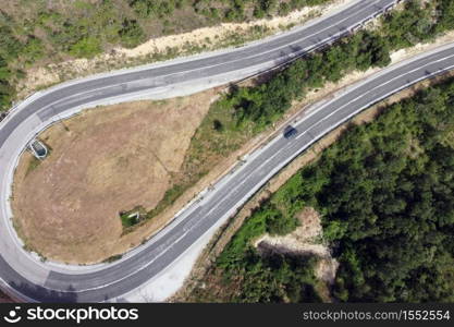 Aerial view of winding road in high mountain pass trough green pine woods. High quality photo. Aerial view of winding road in high mountain pass trough green pine woods.