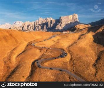 Aerial view of winding road in mountain pass at sunset in autumn. Passo Giau, Dolomites, Italy. Beautiful roadway, orange grass, cars, alpine meadows, sky with clouds. Landscape with highway in fall