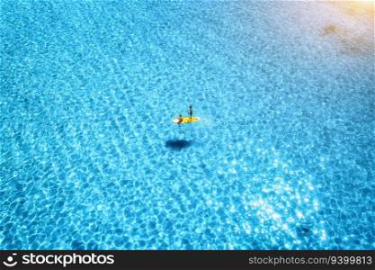 Aerial view of with man and woman on sup board in blue sea at sunset in summer. People on floating canoe in transparent water. Kayak. Sardinia island, Italy. Tropical seascape. Active travel. Top view