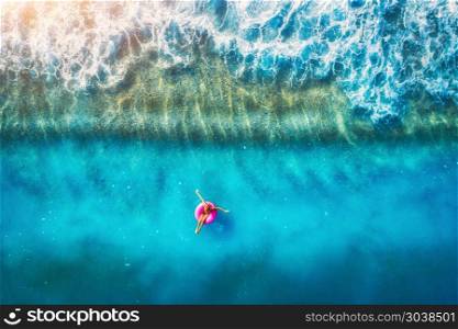 Aerial view of woman swimming on the pink swim ring in the transparent sea in Oludeniz. Summer seascape with girl, beach, beautiful waves, blue water at sunset. Top view. Travel and holiday. Resort. Aerial view of young woman swimming on the pink swim ring