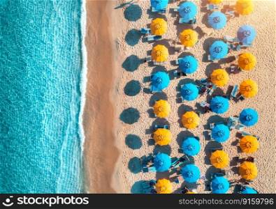 Aerial view of yellow and blue umbrellas on empty sandy beach, blue sea at sunset in summer. Tropical landscape with turquoise water. Travel and vacation in Sardinia, Italy. Top view from drone