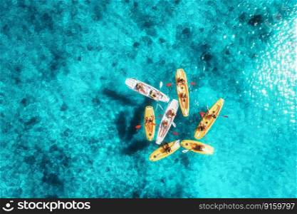 Aerial view of yellow kayaks in blue sea at summer sunny day. People on floating canoes in clear azure water. Sardinia island, Italy. Tropical landscape. Sup boards. Active travel. Top view from drone