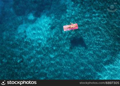 Aerial view of young woman swimming on the pink inflatable mattress in the transparent turquoise sea in Ichmeler,Turkey. Summer seascape with girl, azure water in the morning. Top view from drone. Aerial view of young woman swimming on the pink inflatable mattr