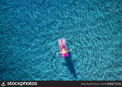 Aerial view of young woman swimming on the pink inflatable mattress in the transparent turquoise sea in Ichmeler,Turkey. Summer seascape with girl, azure water in the morning. Top view from drone. Aerial view of young woman swimming on the pink inflatable mattr