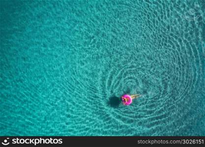Aerial view of young woman swimming on the pink swim ring. Aerial view of young woman swimming on the pink swim ring in the transparent turquoise sea at sunrise in Thailand. Summer seascape with girl, clear water in the morning. Top view. Travel and holiday