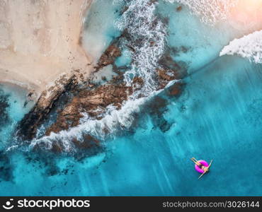 Aerial view of young woman swimming on the pink swim ring in the transparent turquoise sea in Maldives. Summer seascape with girl, beach, beautiful waves, rocks, blue water at sunset. Top view. Nature